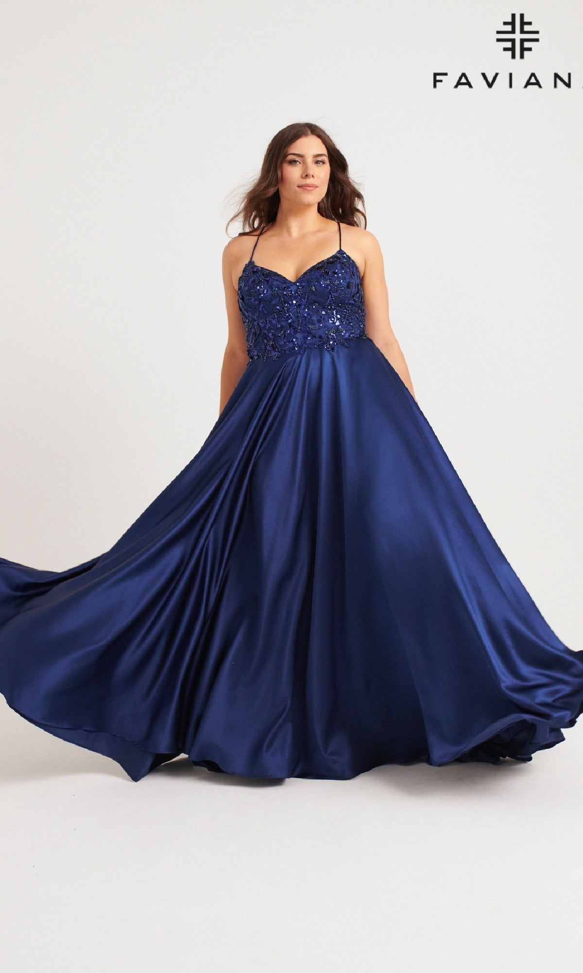 A woman models the Faviana 9578, a deep blue, floor-length satin plus-size prom dress with a sequin embroidered bodice, against a plain backdrop.
